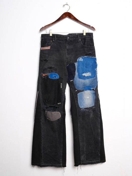 (front): Black Selvedge Patchwork Jeans – front on hanger, faded black wide-leg jeans with heavy blue denim patchwork, hand-stitched repairs and white side seam detail, upcycled – Lillies Studios