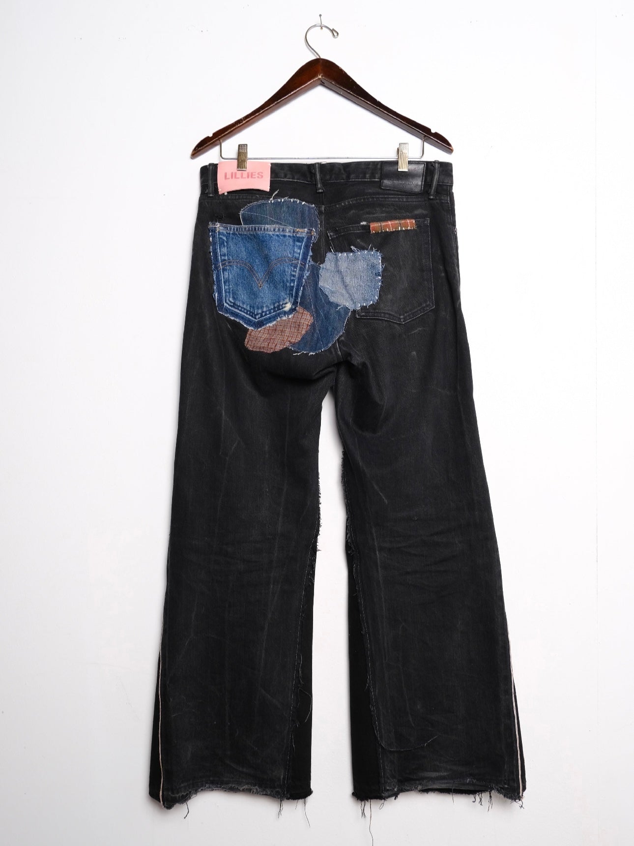 (back): Black Selvedge Patchwork Jeans – back on hanger with Lillies Studios pink label, faded black wide-leg jeans with blue and brown denim back pocket patchwork, upcycled – Lillies Studios